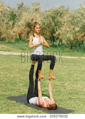 Girl in white shirt exercises yoga outdoor, on green grass. Blue sky on the background.