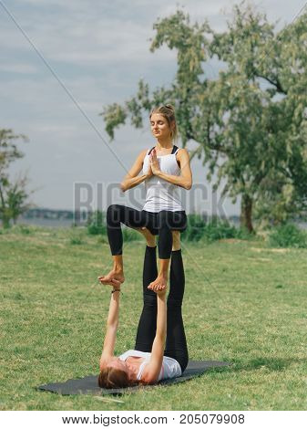 Girl in white shirt exercises yoga outdoor, on green grass. Blue sky on the background.