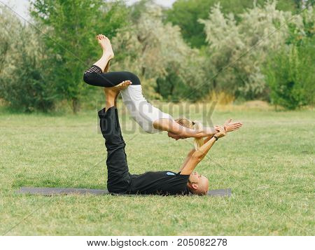 Girl in white shirt exercises yoga outdoor, on green grass. Blue sky on the background.