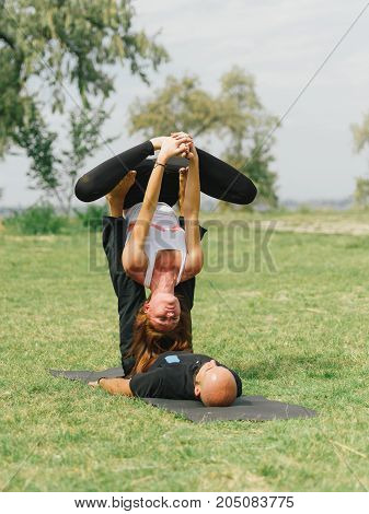 Women doing stretching workout in park outdoors at sunset. Beautiful woman and man practise yoga pose outside.