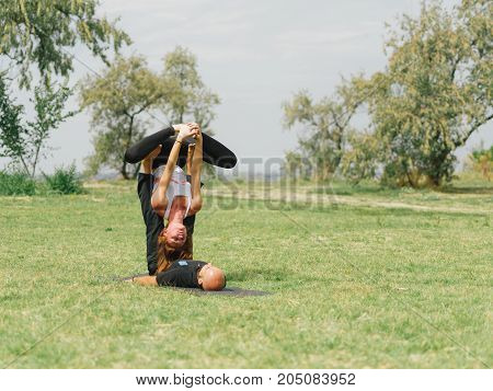 Women doing stretching workout in park outdoors at sunset. Beautiful woman and man practise yoga pose outside.