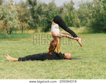 Women doing stretching workout in park outdoors at sunset. Beautiful woman and man practise yoga pose outside.