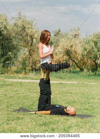 Women doing stretching workout in park outdoors at sunset. Beautiful woman and man practise yoga pose outside.