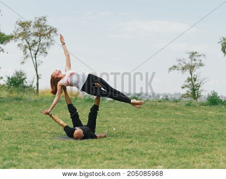 Women doing stretching workout in park outdoors at sunset. Beautiful woman and man practise yoga pose outside.