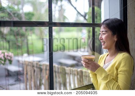 Asian woman is enjoying with coffee break and looking to outside window of coffee shop.