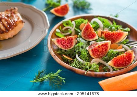 Autumn salad of arugula, figs in a brown earthenware plate on a dark background.