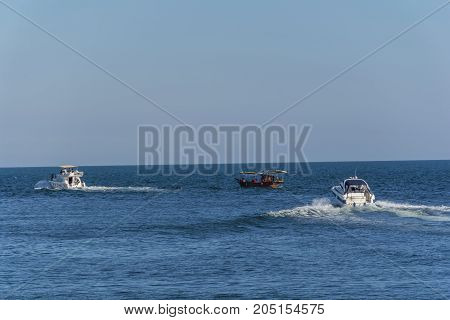Three boats moving through the blue wather. Luxury private motor yacht under way on Black Sea sea with bow wave. People ride in wooden boat.