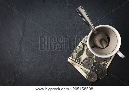 Empty coffee cup with one dollar bill and some coins on grey background