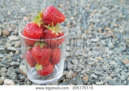 Glass full of red ripe strawberries stands on the grey crushed stones.