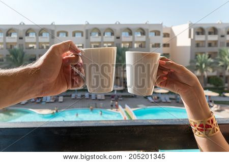 The Hands Of Men And Women Keep Coffee Mugs On The Balcony In The Background Of The Hotel, Where The