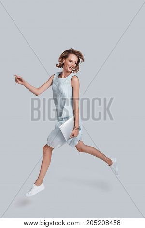 Mid-air motion. Full length of playful young woman gesturing and smiling while jumping against grey background