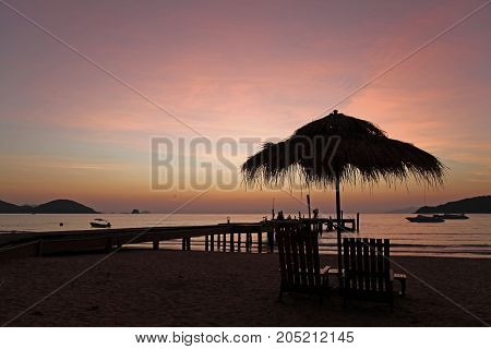 relax with beautiful sunset in the evening bridge chair beach bar beach umbrella boat silhouette at Koh Mak Trad Thailand