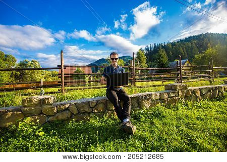 Young man works at laptop outdoor in the mountains at sunset