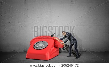 A small businessman fails to destroy a large red retro phone with a broken hammer. Too many calls. Need for optimization. Time wasters.
