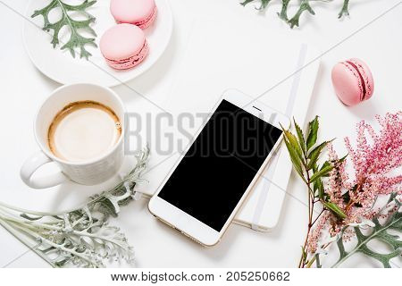 Social media flat lay with coffee, pink macaroons, flowers and smartphone on white background