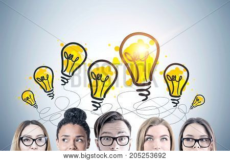 Close up of heads of young people s heads. They are standing near a gray wall with glowing yellow light bulbs drawn on it. A diverse business team. Toned image
