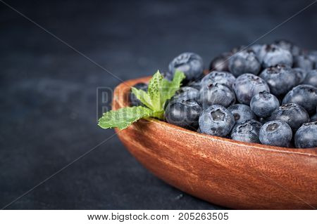 Fresh blueberries with a leaf of mint in the heart-shaped bowl on a dark blue background