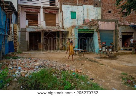 Agra, India - September 20, 2017: Two beautiful litle girls saying hello to the camera of a foreign tourist, surrounding of old building houses, over a stoned ground, in the street in Agra city in India.
