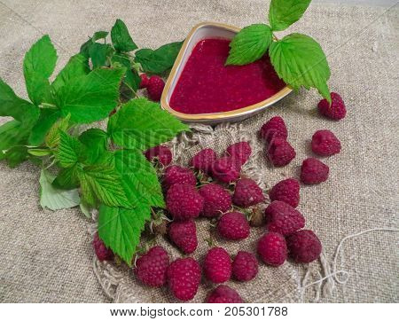 scattered on the table ripe fresh berries of raspberries along with jam.