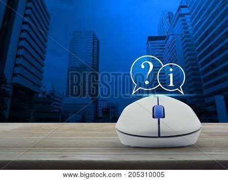 Question mark and information chat icon with wireless computer mouse on wooden table over modern office city tower Customer support concept