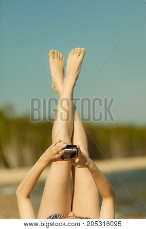 Summertime pleasures enjoying vacation concept. Woman in bikini sunbathing and relaxing on beach using smartphone checking social media and writing sms
