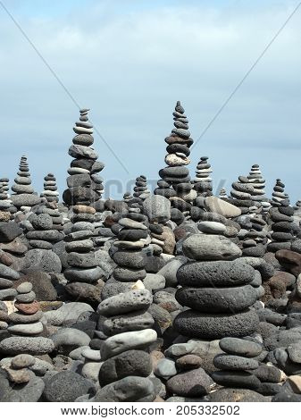 rock art piles and towers of grey stones and pebbles on a beach with blue sky
