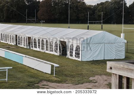 Big white banquet tent with windows near the green fields and tree.