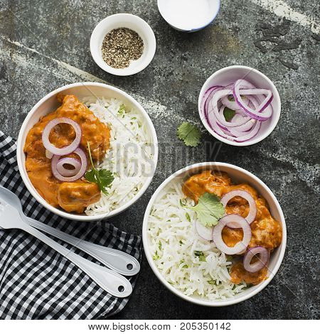 Homemade dinner butter chicken on cream with spices, cream served with basmati rice in ceramic bowls with cilantro and sweet red onion. Top View