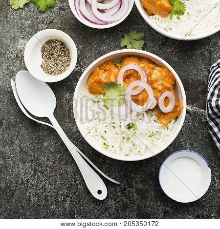 Homemade dinner butter chicken on cream with spices, cream served with basmati rice in ceramic bowls with cilantro and sweet red onion. Top View
