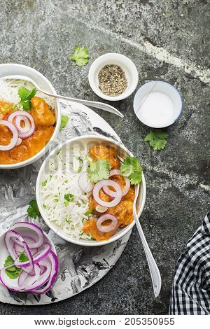 Homemade dinner butter chicken on cream with spices, cream served with basmati rice in ceramic bowls with cilantro and sweet red onion. Top View