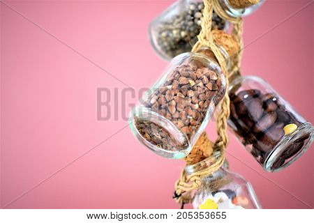 Collection of grain products, lentils, soybeans and red beans in storage jars over on free background. Quinoa, bulgur and couscous cereals. Vegetarian and dieting food concept. Cereals in glass jars are amused by a linen lace on is dusty a pink background
