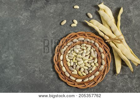 Bunch of white string beans tied with twine and bean grain on round wicker tray. Long white pods and tray on gray textured background. New harvest. Ingredient in healthy and dietary food. Top view