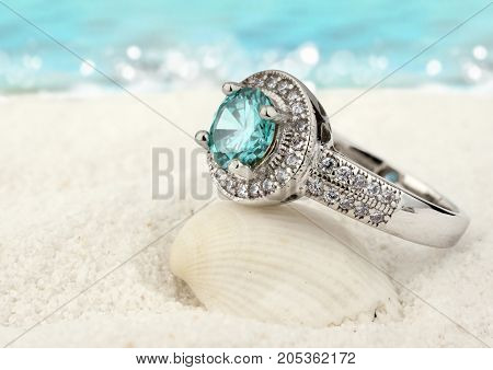 Jewelry ring with aquamarine gem on sand beach background