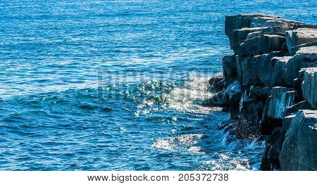 Illuminated waves splashing against edge of rocky breakwall in shadow.
