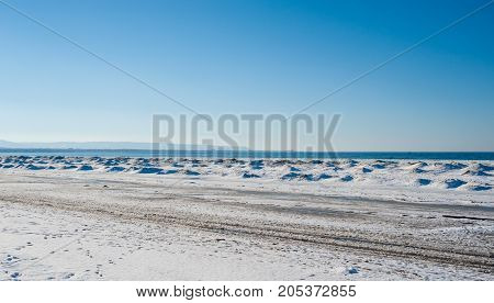 Frozen ice and sand dunes on beach in winter by lake under clear blue sky near Georgian Bay Ontario Canada.