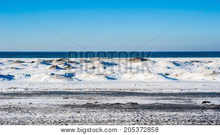 Frozen ice and sand dunes on beach in winter by empty lake horizon under clear blue sky near Georgian Bay Ontario Canada.