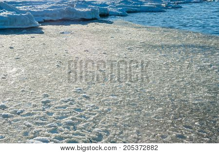 Melting chunks of ice floating into water near frozen shore.
