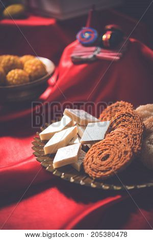 stock photo showing Diwali still life with Diya or oil Lamp, gift boxes, sweets and fire crackers with flowers arranged over red satin cloth with bokeh