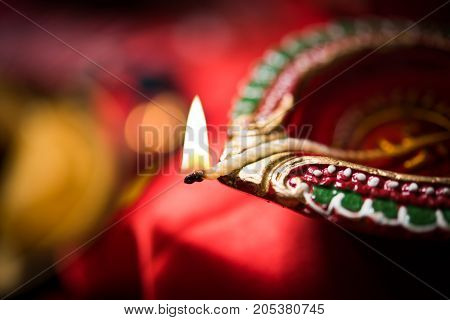 stock photo showing Diwali still life with Diya or oil Lamp, gift boxes, sweets and fire crackers with flowers arranged over red satin cloth with bokeh