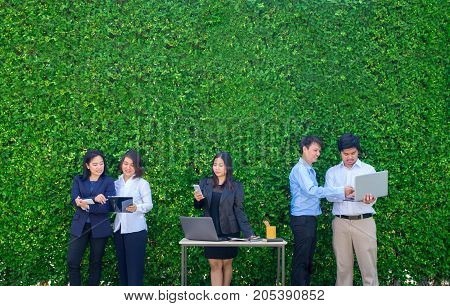 Businesswoman and businessman working outside office using laptop computer mobile phone and tablet device at green leaf wallmobile office conceptcopy space for adding text or designSquare banner.