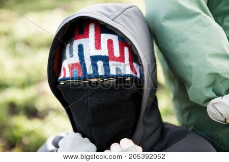 masket person with sunglasses and hood looking in to the camera