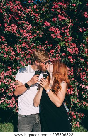Couple in park eating ice cream cones, posing on camera