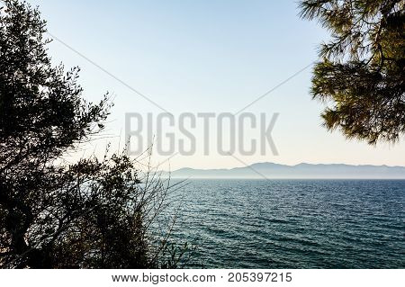 Landscape of open sea with green vegetation canopy of the pine tree islands are far away in background.