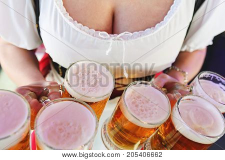 Girl in a traditional dress with a big breasts and deep neckline holds full mugs of beer during the celebration of the Oktoberfest