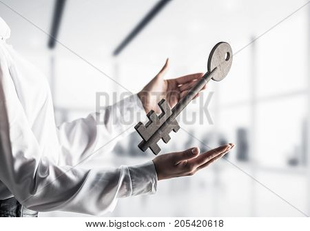 Business woman in white shirt keeping big stone key in hands with office view on background. Mixed media.