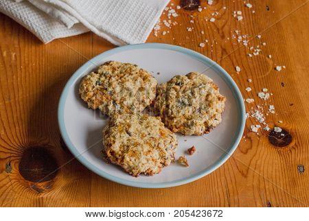 Homemade sweet and crunchy oats cookies on rustic bright wooden kitchen table with oats and white cloth - Food background