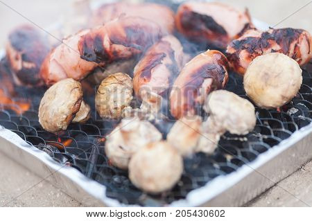 feeding, vacation, cooking concept. luscious close up of barbecue with deep fried suasage and delicious champignons, they fried on black grill in the garden