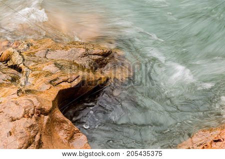harmony, travelling, nature concept. there is soft and graceful waves of green waters that floating very fas, they are washing over textured orange stones of rocky coast