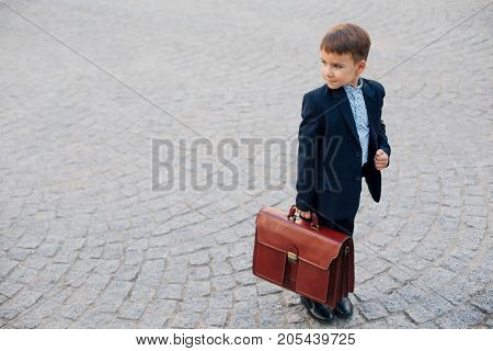 Concept future businessman. High angle of businessman in formal wear standing on pedestrian street carrying a braun briefcase looking to right, urban gray pavage stone background. Copy space.