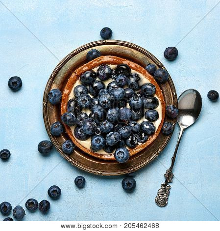 Blueberry tart, pie, tartlet with custard on blue stone background.
